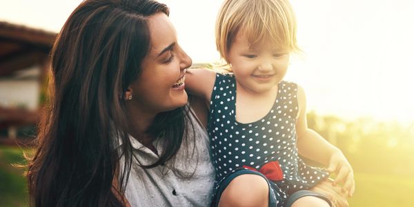 Mother laughing joyfully with her toddler in a sunny outdoor setting.
