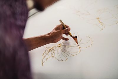An artist painting delicate floral patterns on fabric with a brush.