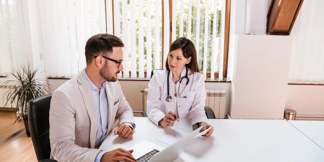 Doctor consulting with a patient using a laptop in a bright office.