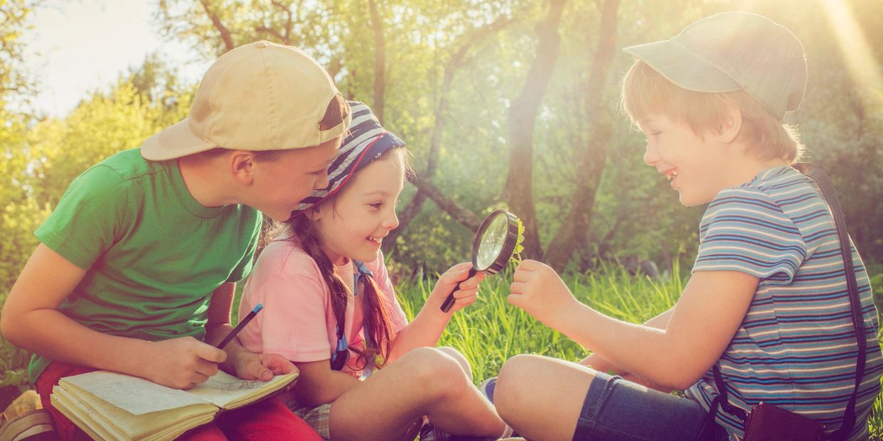 Three kids exploring nature with a magnifying glass.