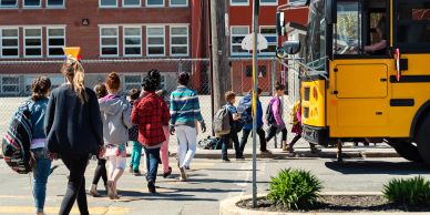 Children boarding a yellow school bus outside a school.