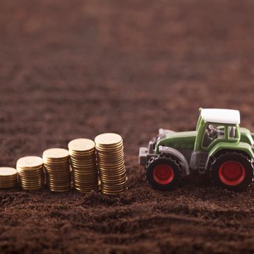 Toy tractor next to stacks of coins on soil representing agricultural finance.