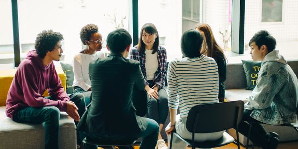 A diverse group of young adults engaged in a discussion in a bright room.