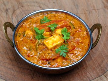 Paneer curry garnished with fresh cilantro in a traditional metal bowl.