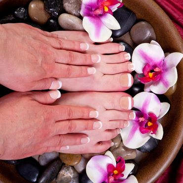 Hands and feet with French manicure and pedicure surrounded by orchids and smooth stones.