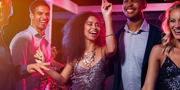 Group of friends joyfully dancing and laughing at a party with vibrant lighting.