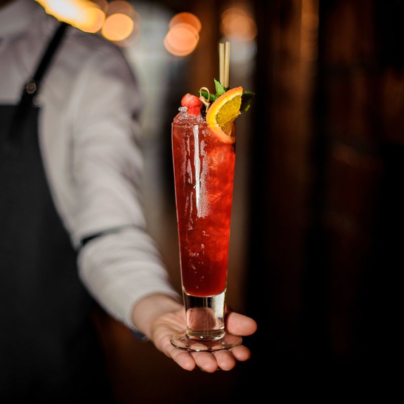 Bartender holding fresh red cocktail in the glass decorative with a mint, strawberries and lemon