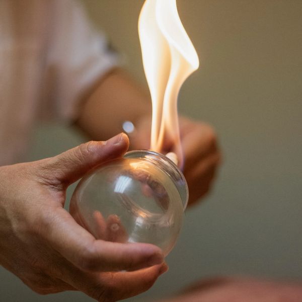 Person holding a glass fire cupping jar with flames.