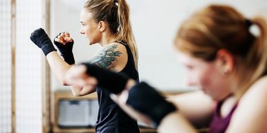 Two women practicing boxing punches indoors, focused and determined.