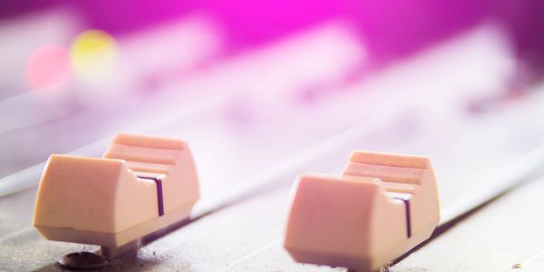 Close-up of audio mixer sliders with pink lighting and bokeh effect.