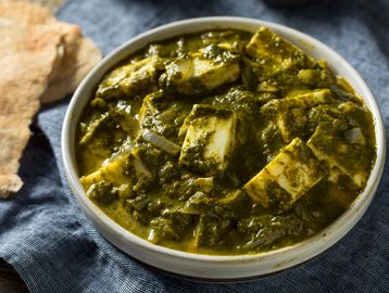 A bowl of palak paneer curry with flatbread on the side.