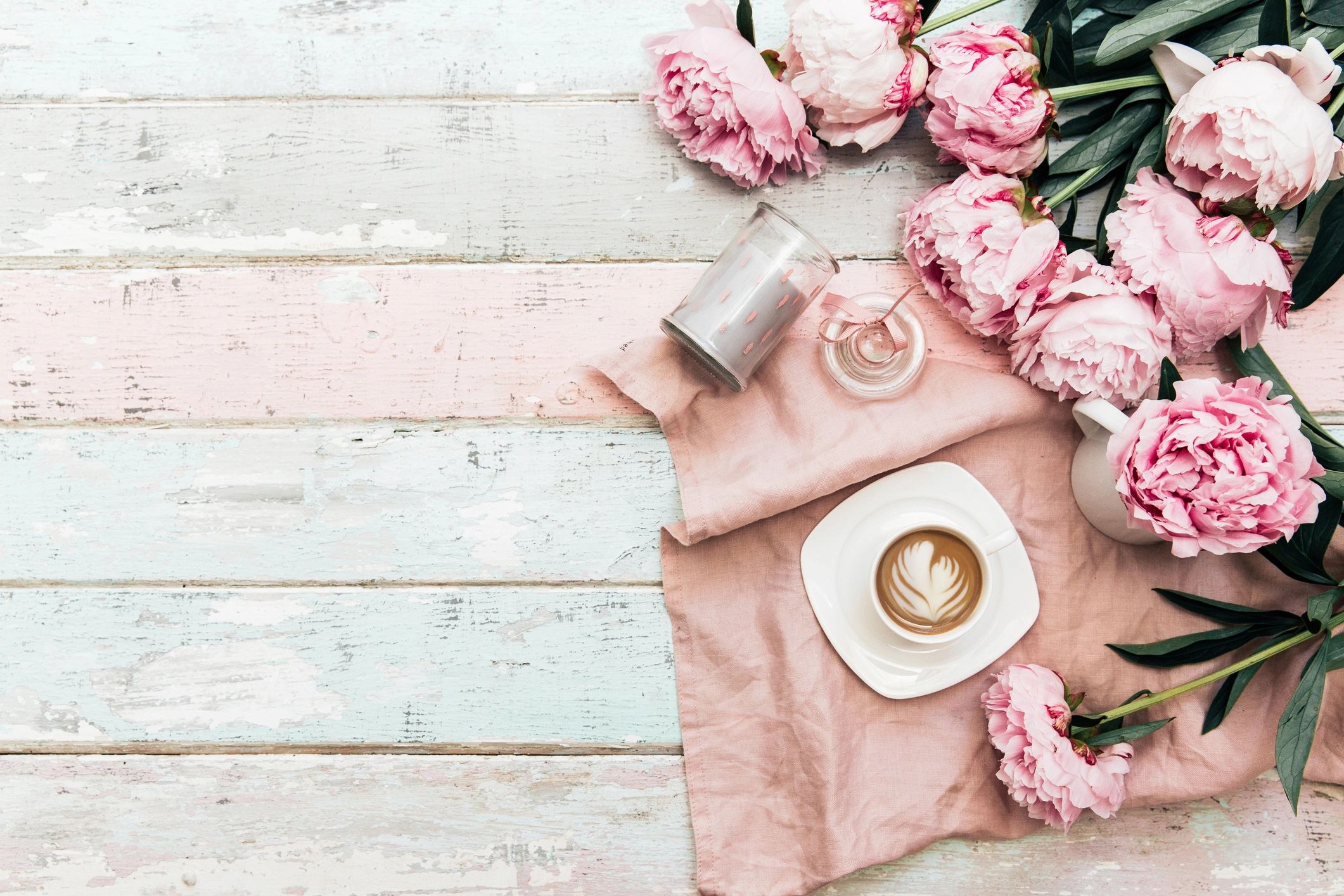 Coffee with pink peonies and a candle on a wooden table.