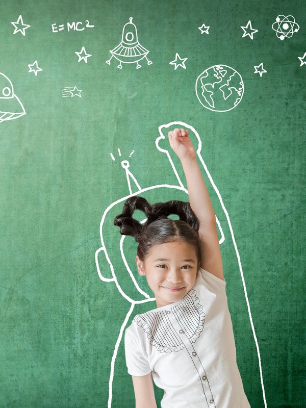 A smiling girl posing with space-themed chalk drawings on a green chalkboard.