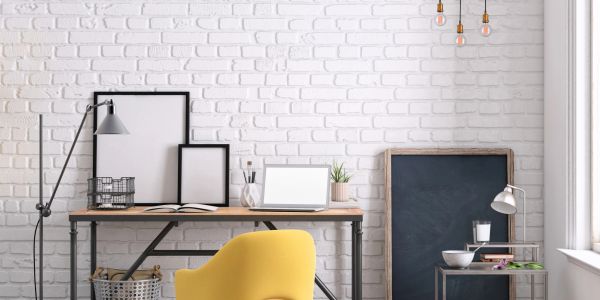 Minimalist workspace with a yellow chair and white brick wall.