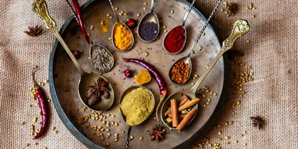 Various colorful spices and herbs in spoons arranged on a round metal tray.