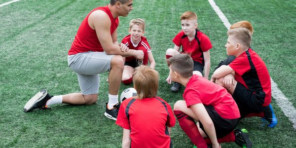 Coach giving a pep talk to young soccer players on the field.