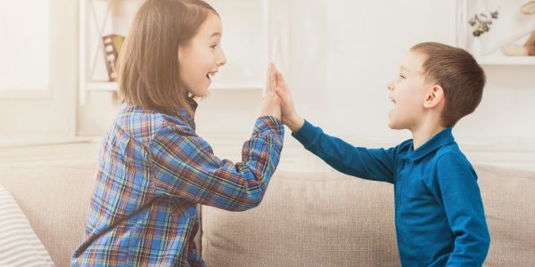 Two children high-fiving joyfully on a couch.