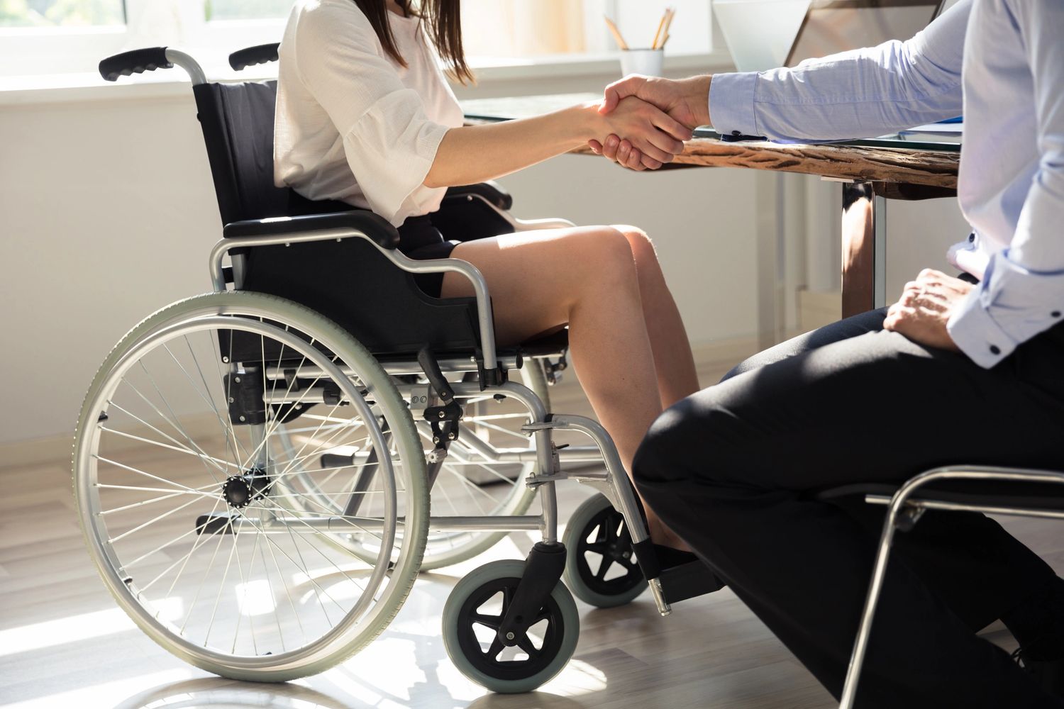 A woman in a wheelchair shaking hands with a man across a table.