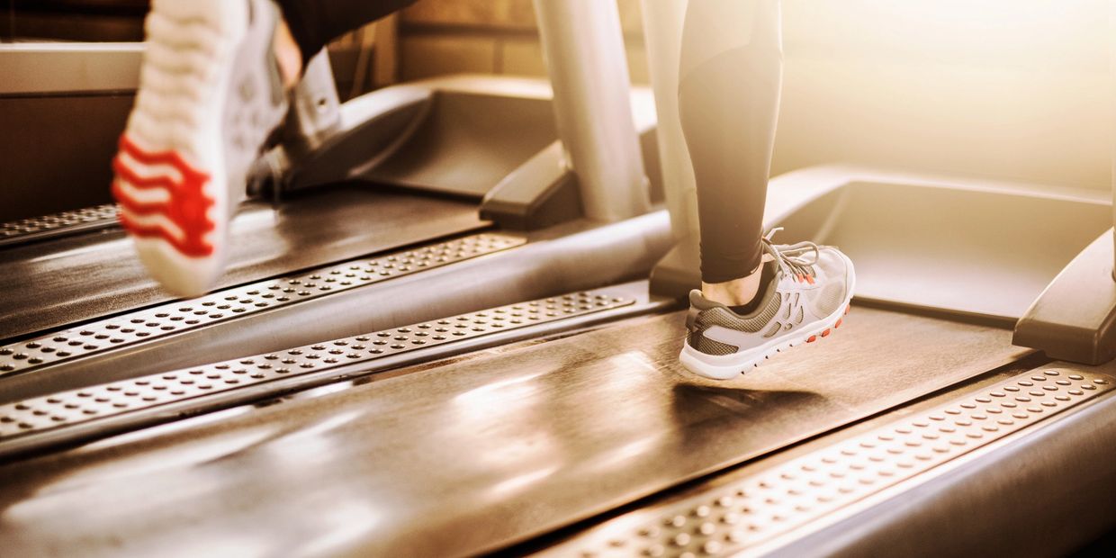 Close-up of a person running on a treadmill wearing gray sneakers with red accents.