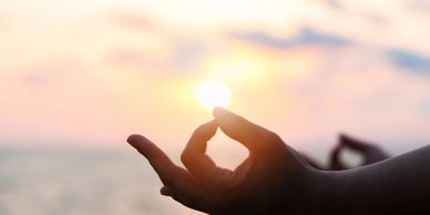 Hand in meditation pose holding the sun during a serene sunset.
