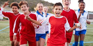 Group of kids in sports uniforms smiling and cheering.