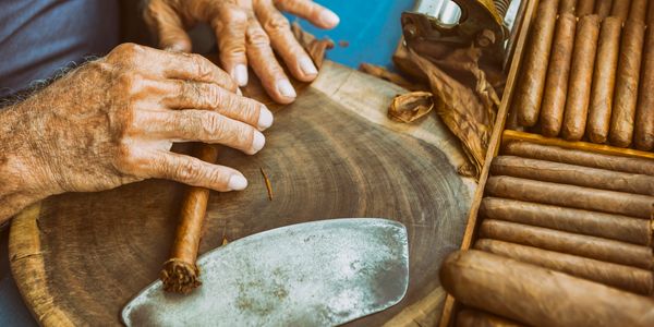 Hands rolling a cigar on a wooden surface with a box of cigars nearby.