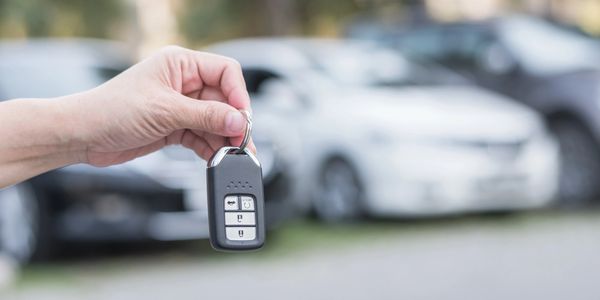 Hand holding a car key fob with blurred cars in the background.