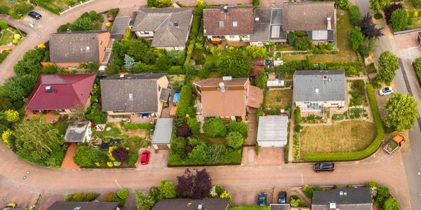 Aerial view of suburban houses with gardens and cars parked on the street.