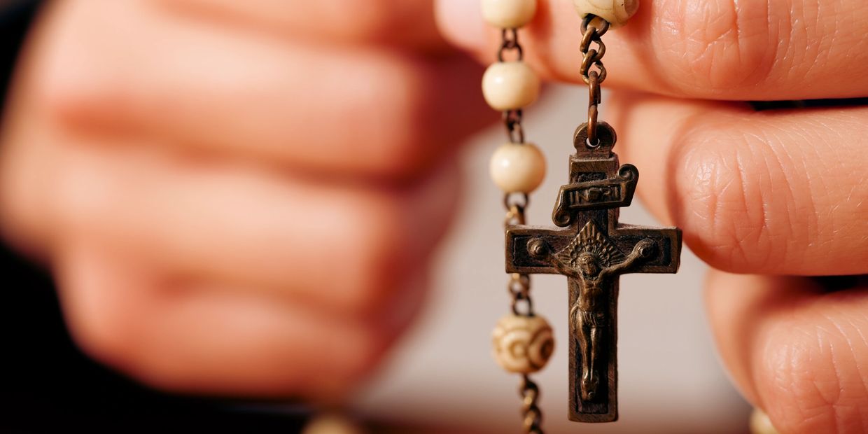 Close-up of hands holding a rosary with a crucifix.