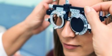 Optometrist adjusting trial frames on a young woman's face during an eye exam.