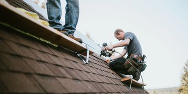 Two workers installing solar panels on a rooftop under clear sky.
