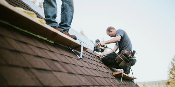 Two workers installing solar panels on a roof on a sunny day.