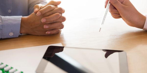Doctor consulting patient with medication and tablet on table.