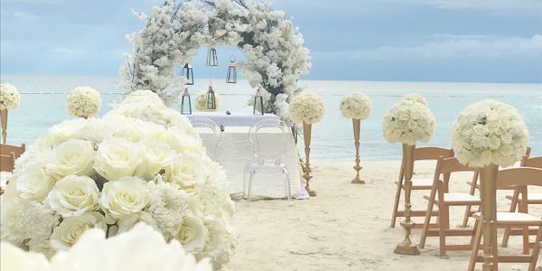 Elegant white floral beach wedding setup with chairs and arch.