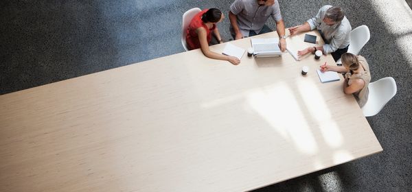 Four people collaborating around a large wooden table in a bright room.