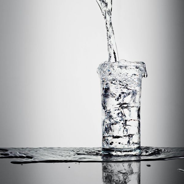 Water is being poured into a glass filled with ice cubes, overflowing slightly.