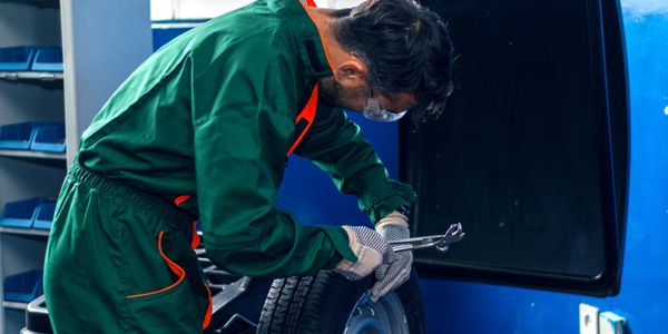 Mechanic in green coveralls repairs a car tire using a wrench in a workshop.