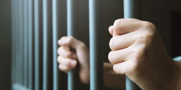 Hands gripping prison bars tightly, symbolizing confinement.