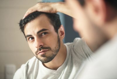 Man examining his hairline in the mirror with concern.