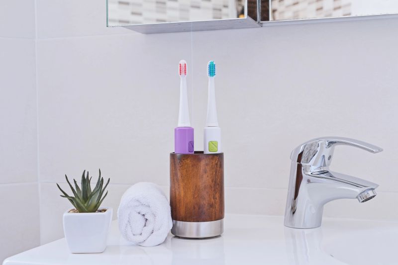Two electric toothbrushes in wooden glass on sink in the bathroom with white wrapped towel. Chrome water tap and sink. Bathroom interior and accessories concept