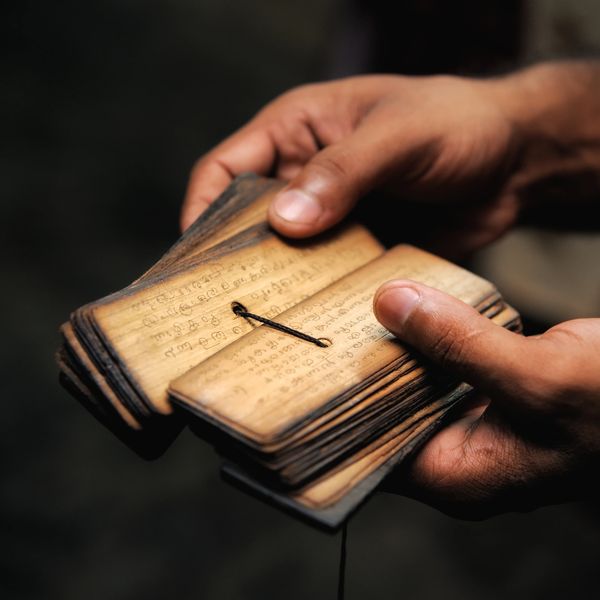 Hands holding ancient palm leaf manuscripts with script.