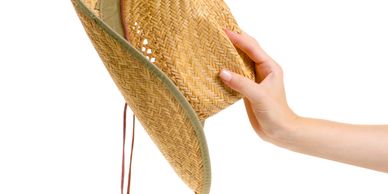 A hand holding a woven straw hat with a green edge.