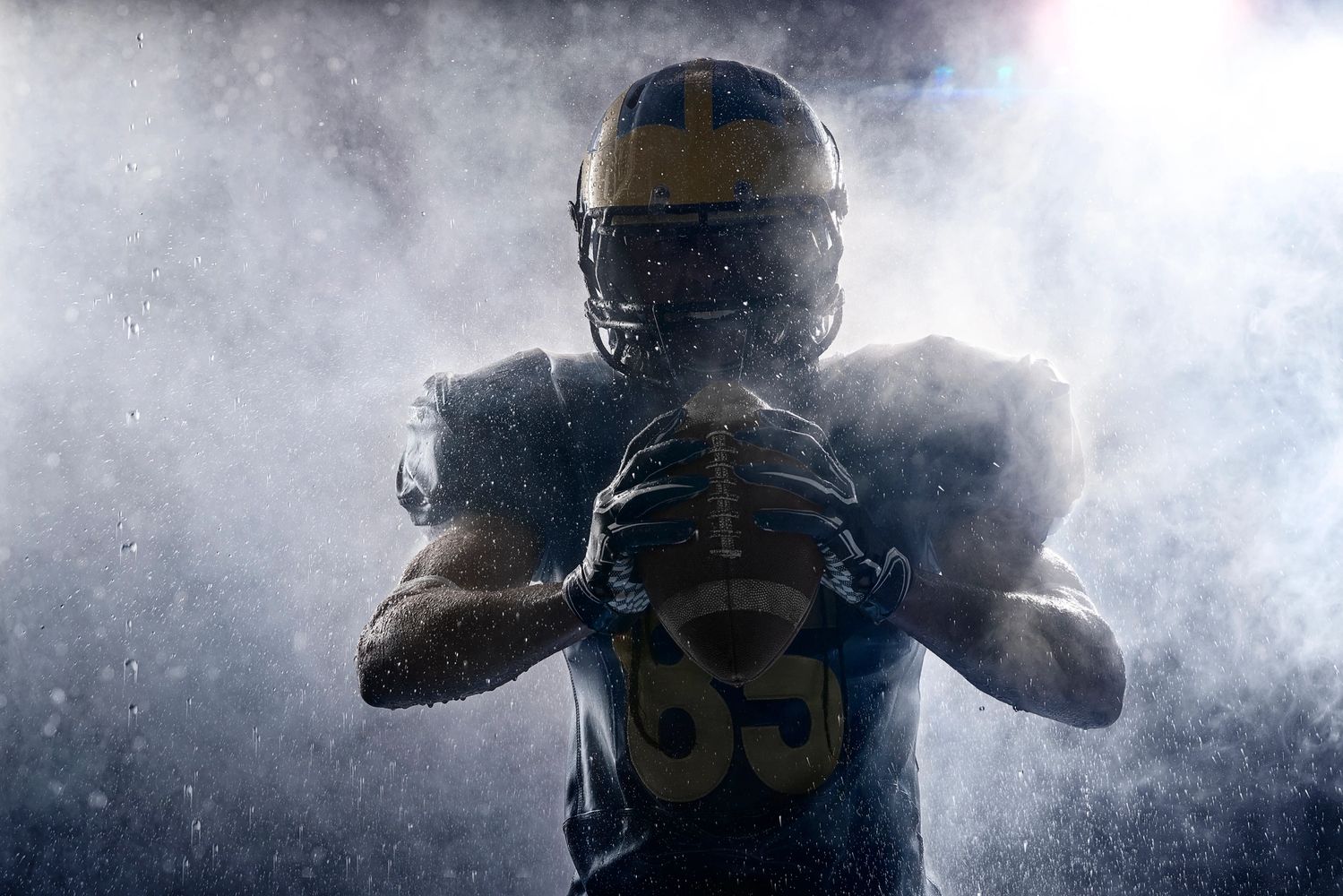 American football player in rain holding a football with dramatic lighting.