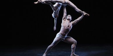 Two dancers perform an impressive acrobatic pose in white costumes with body paint.
