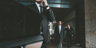 Men in suits walking outside a modern building, one using a phone.