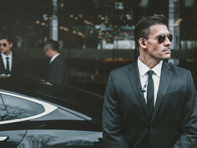 Security agents in suits and sunglasses standing near a luxury black car.