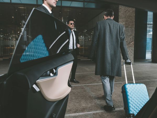 Businessman with luggage approaching a car and a driver waiting.
