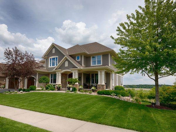 Large suburban home with manicured lawn and mature trees under a cloudy sky.