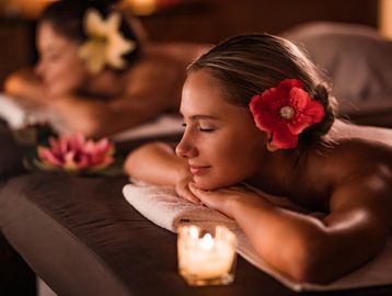 Two women relaxing with flowers in their hair during a spa massage.