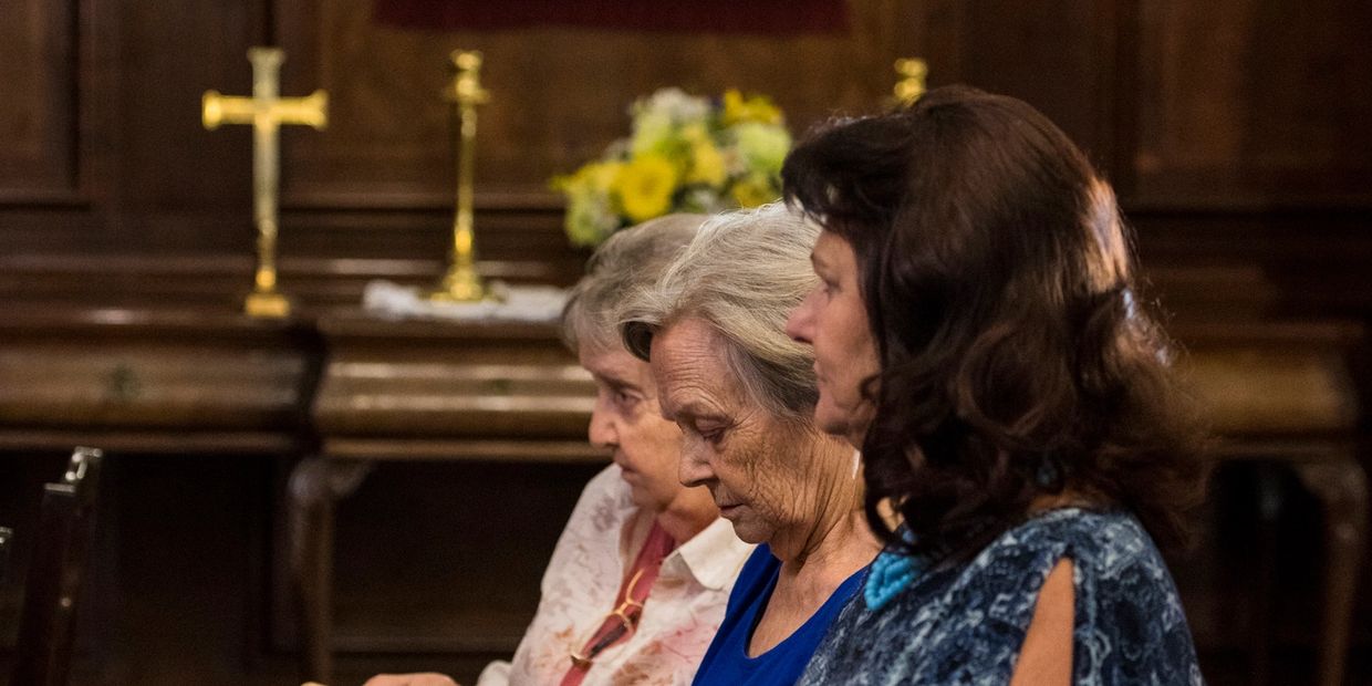 Three women sitting in a church during a service or prayer.
